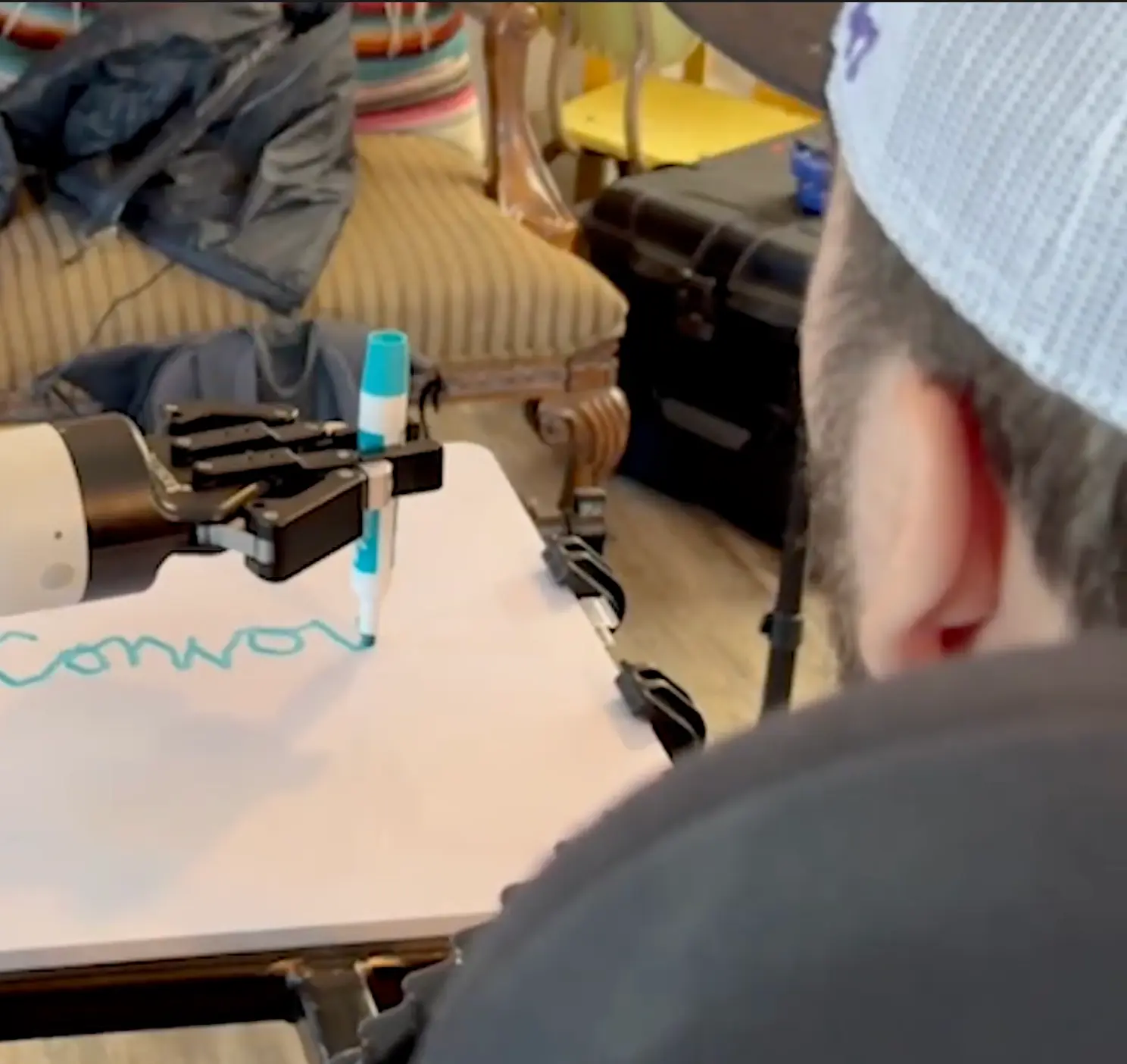 Robot arm holding a marker, which Alex is using to write on a whiteboard