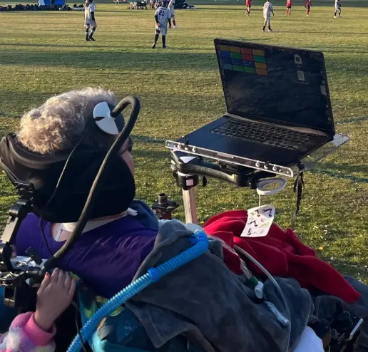 Side view of Brad sitting in a wheelchair, using Neuralink to communicate while outside